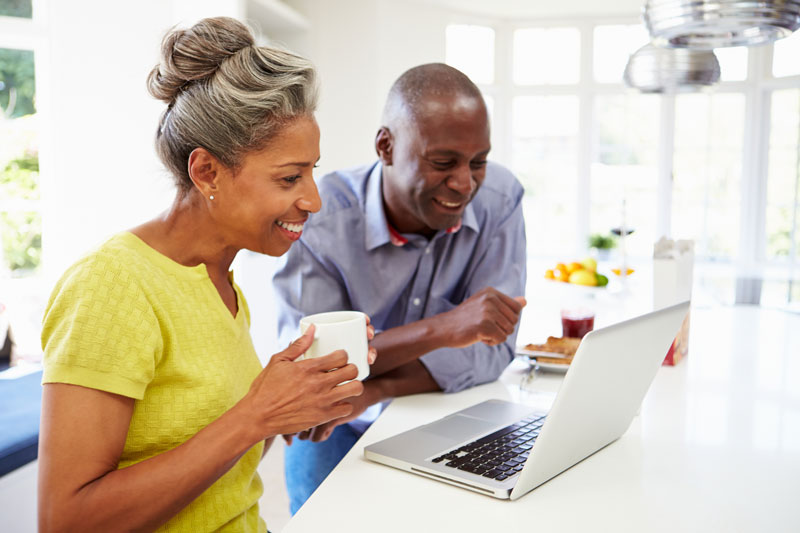 happy couple applying for retirement on laptop in kitchen