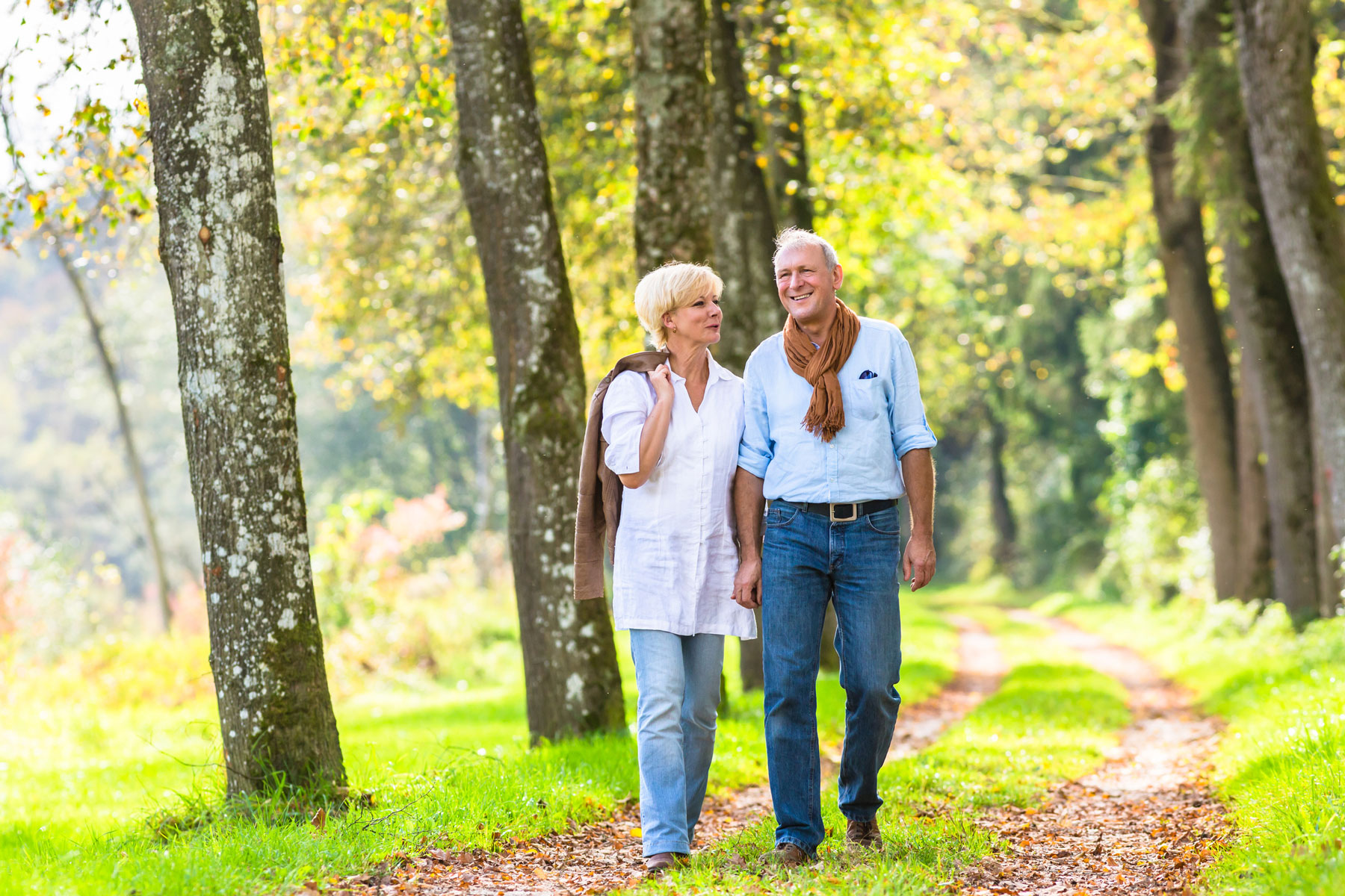 happy retired couple walking on path in woods