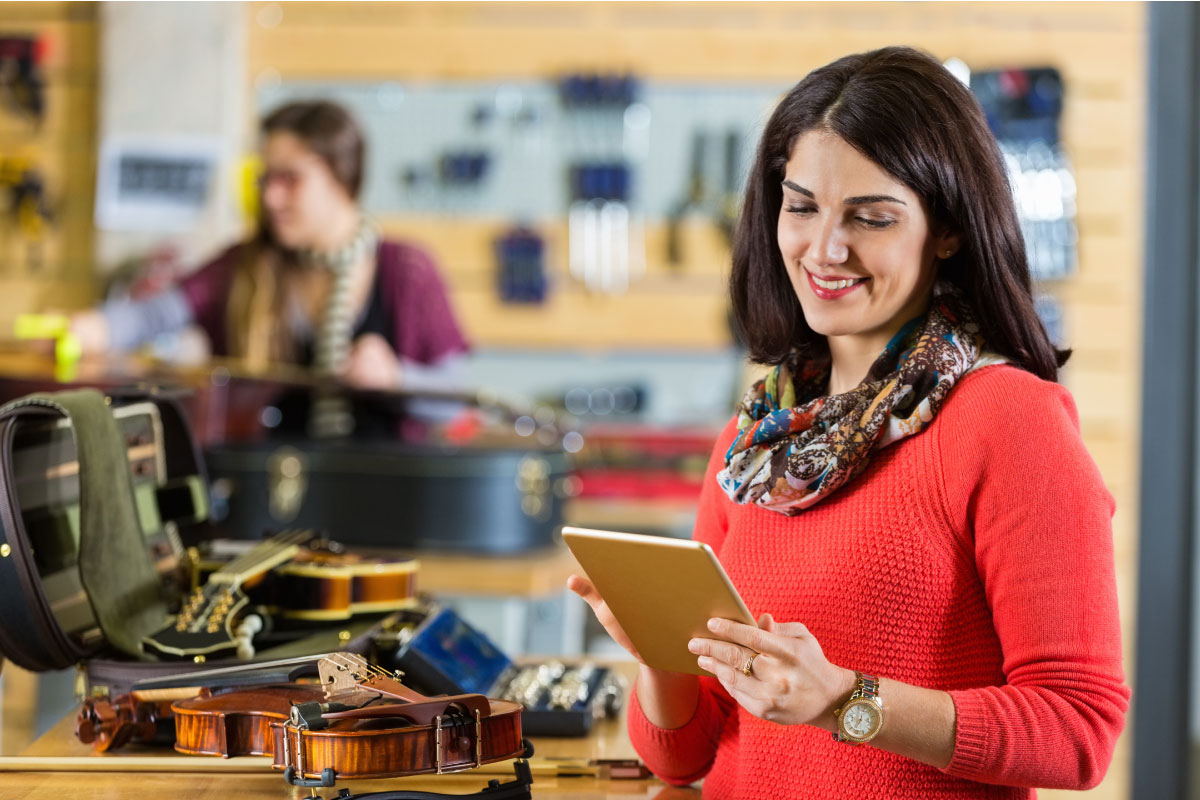 woman in violin store, checking retirement account on tablet device