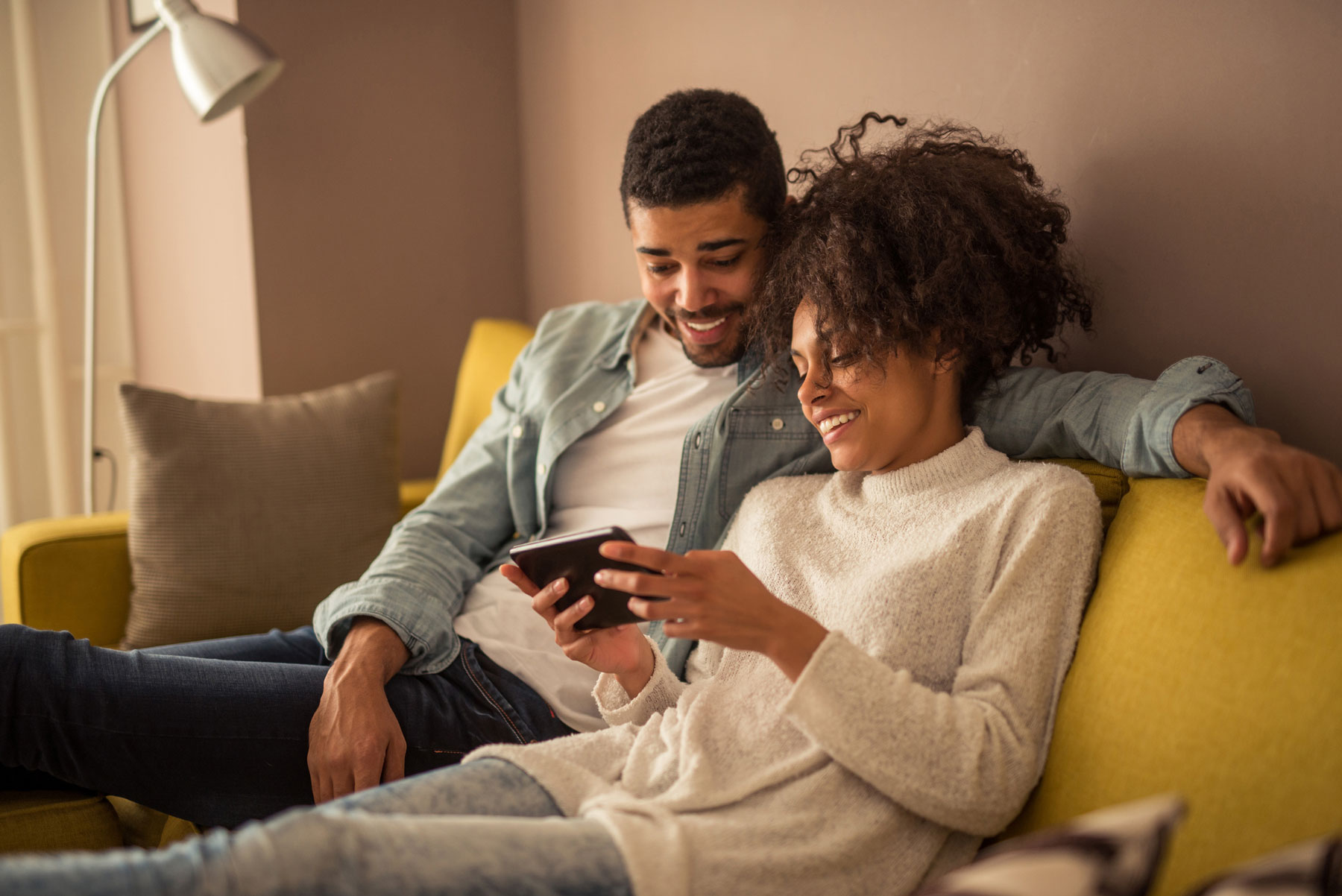 couple on couch, checking retirement plans on tablet device